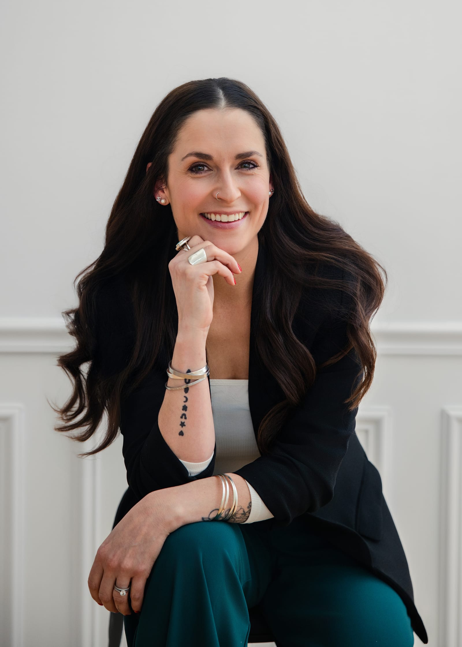 Professional in a teal dress seated on a stool against a white ground
