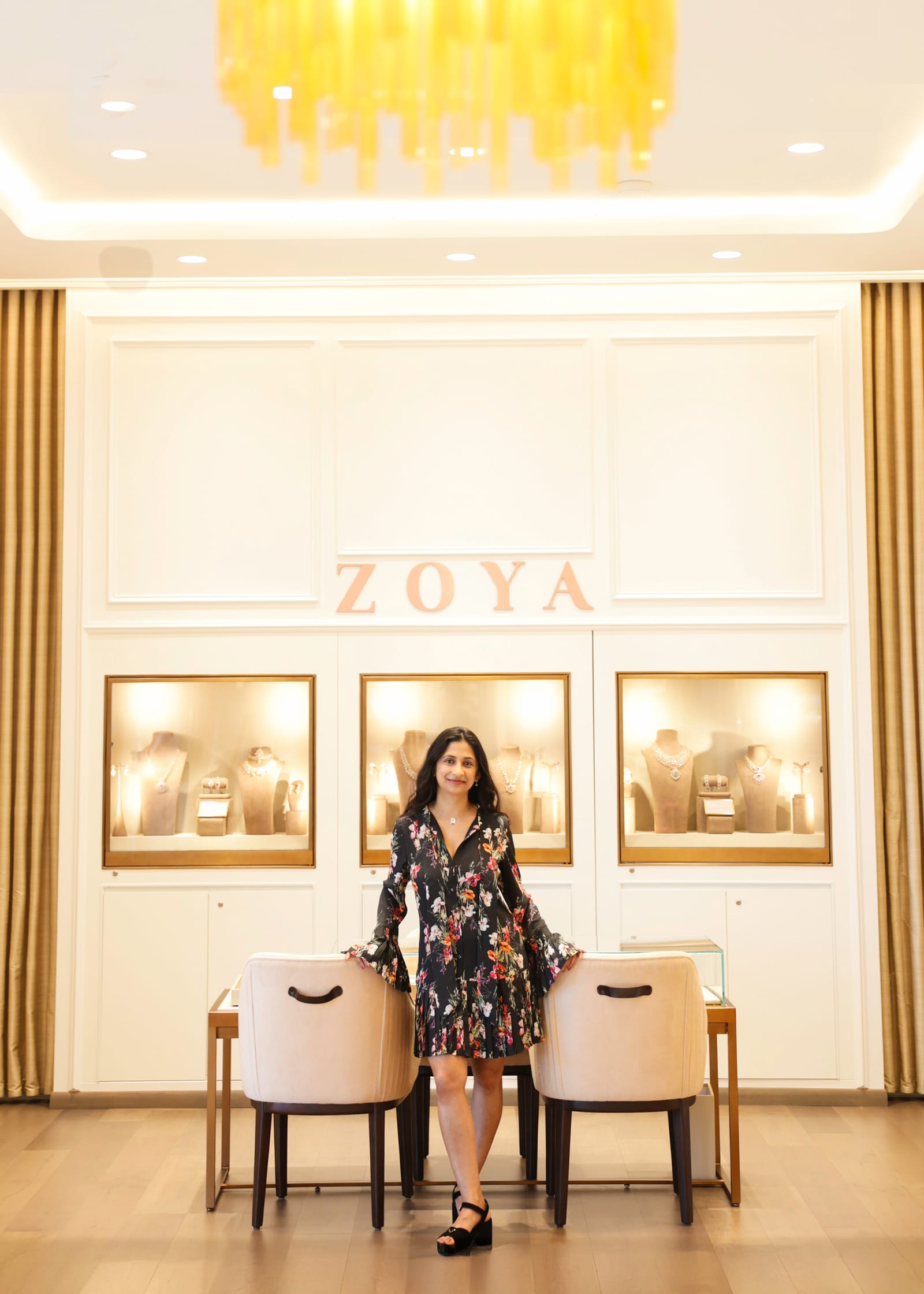 Business owner seated on a pale chair in her softly lit jewellery showroom