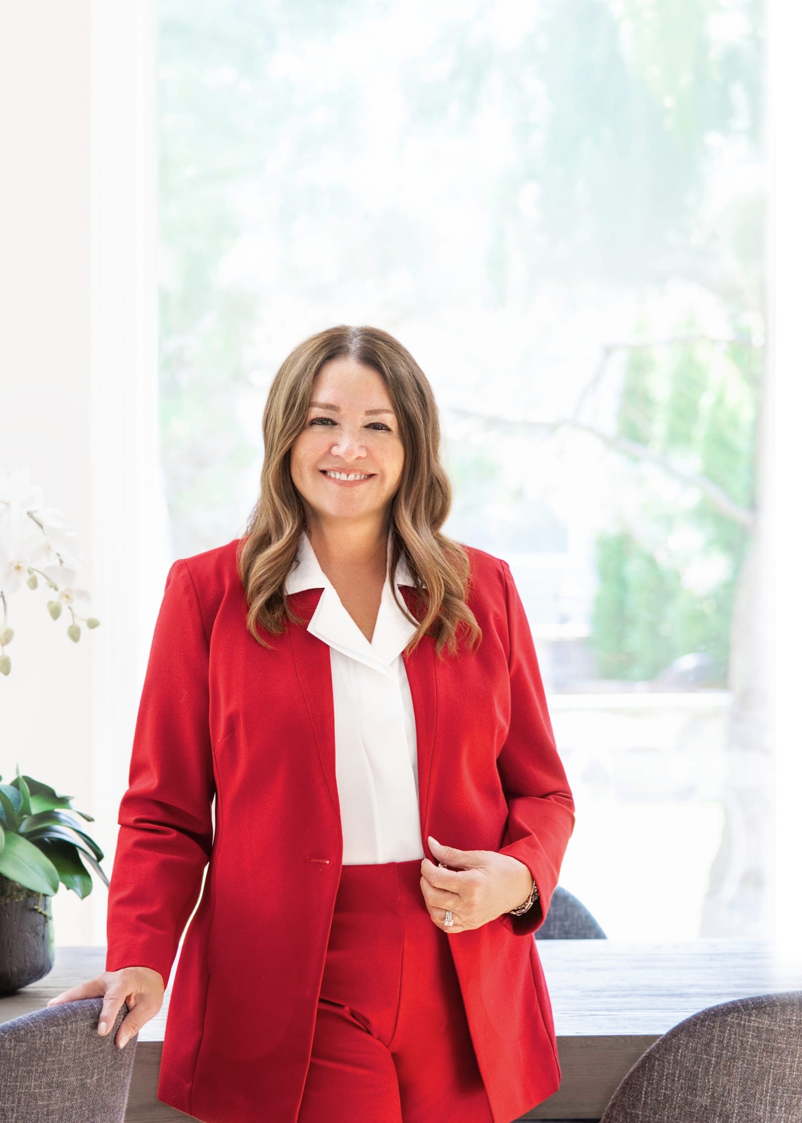 Business owner in a red trouser suit standing beside a bright window