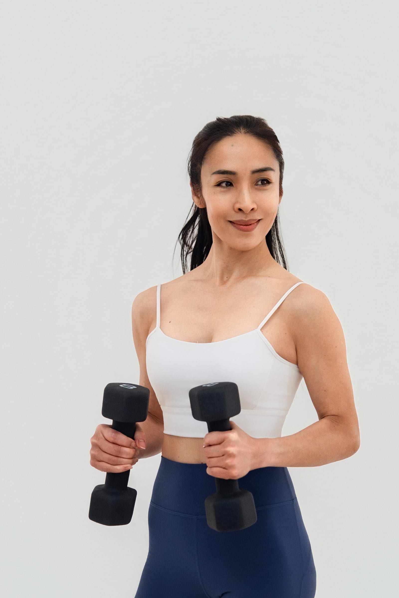 Business owner in white activewear holding a pair of dumbbells against a pale grey wall