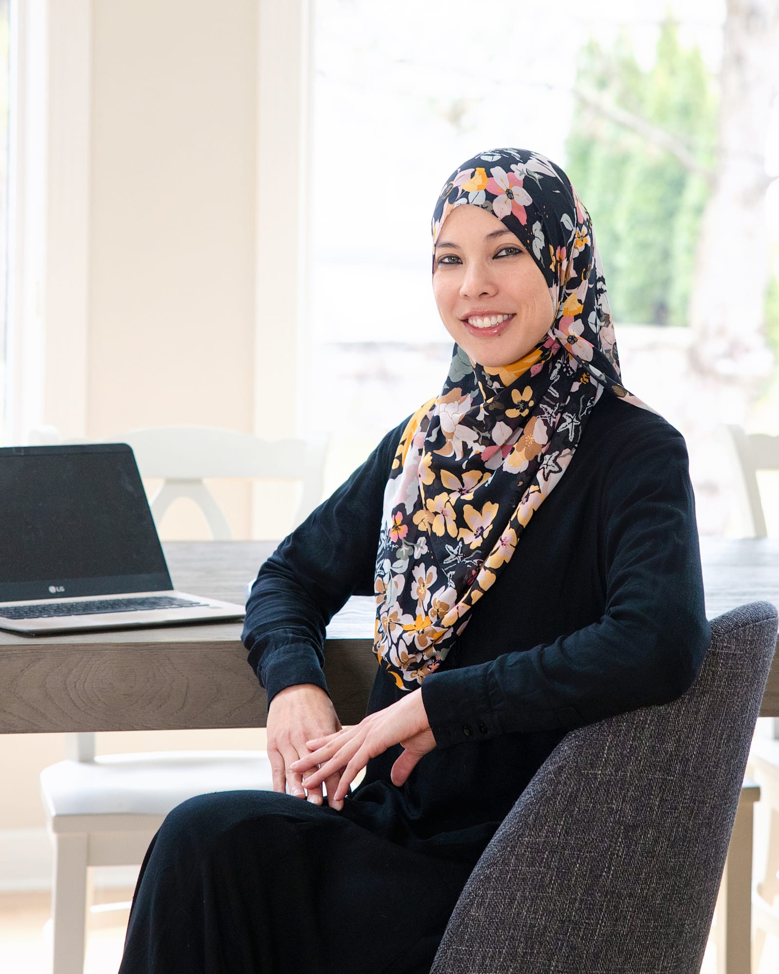 Professional in a patterned headscarf seated at a work table beside a laptop