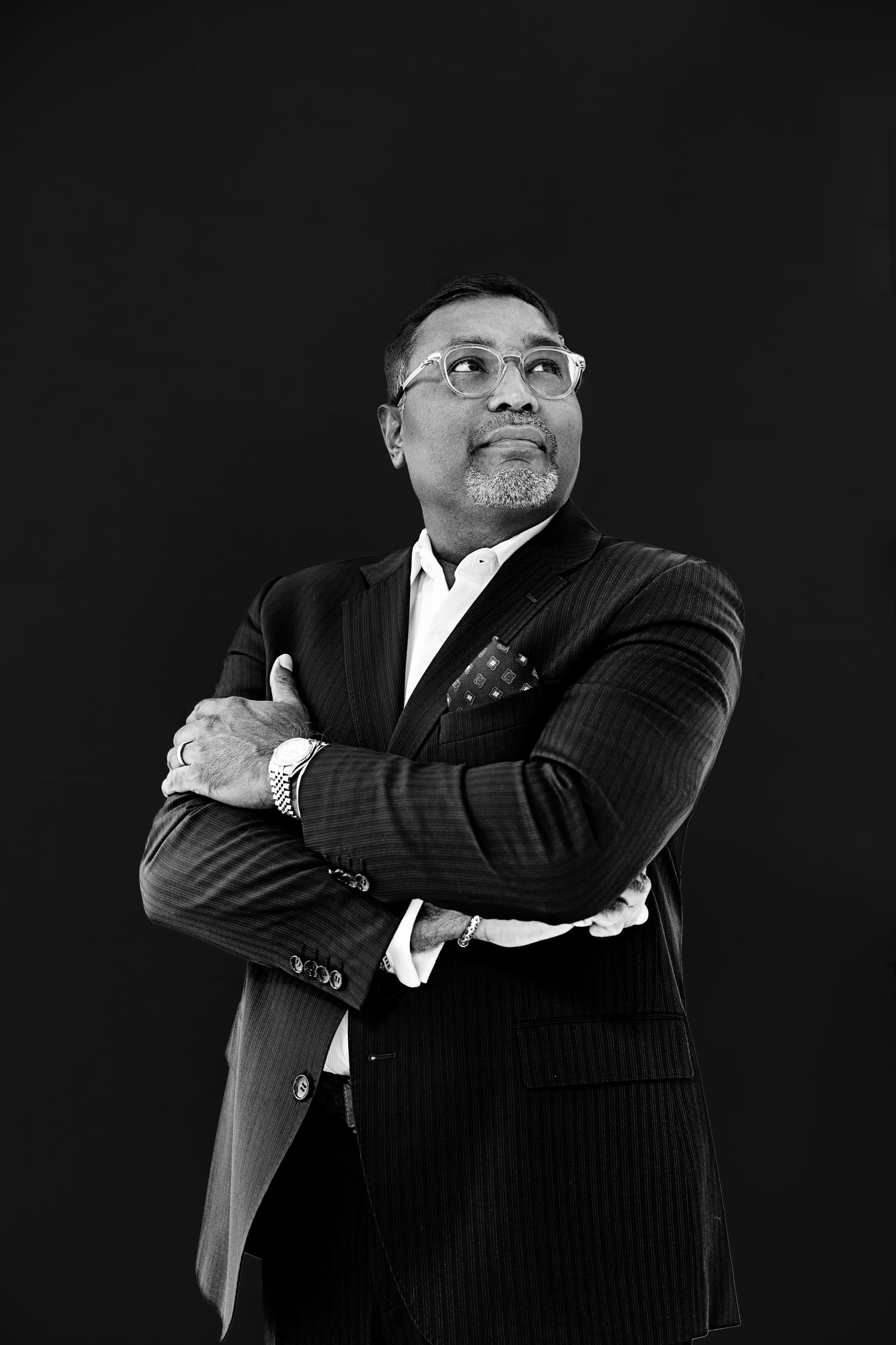 Black and white portrait of an executive in a pinstripe suit with arms crossed, against black