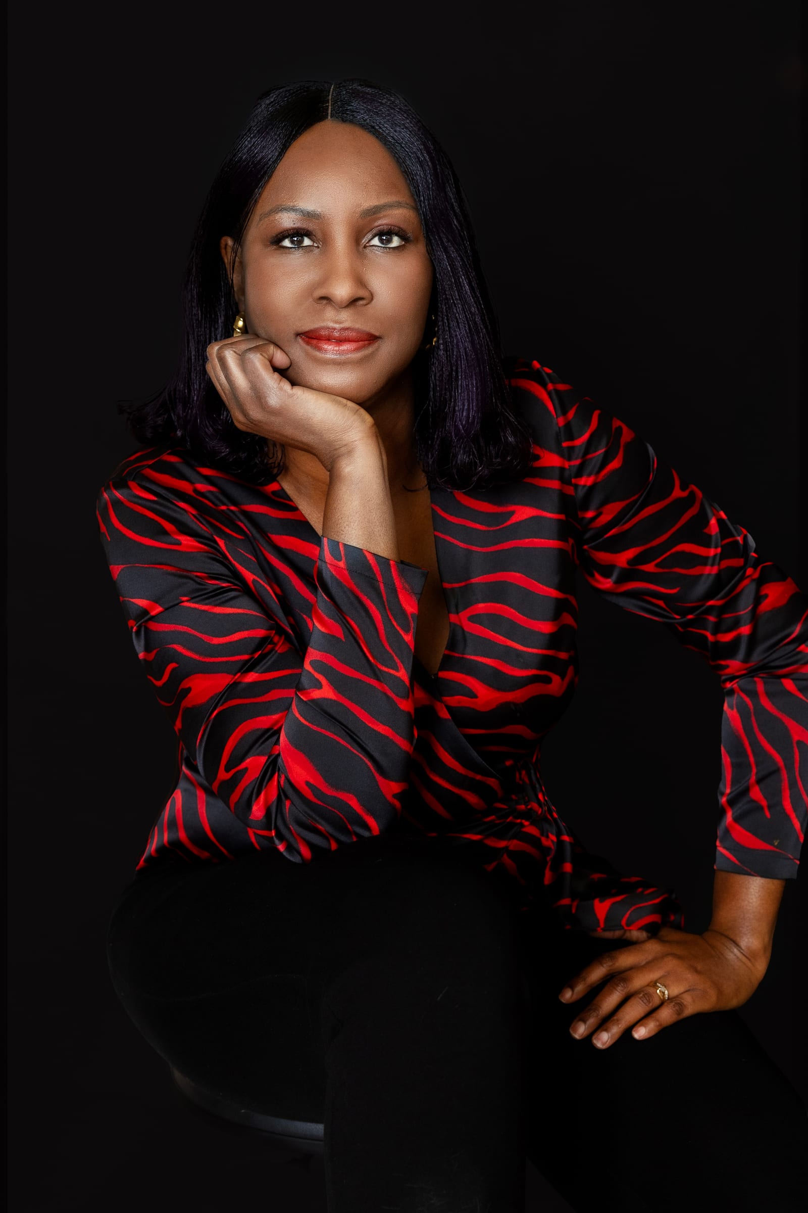 Professional in a red and black patterned jacket resting her chin on her hand against black