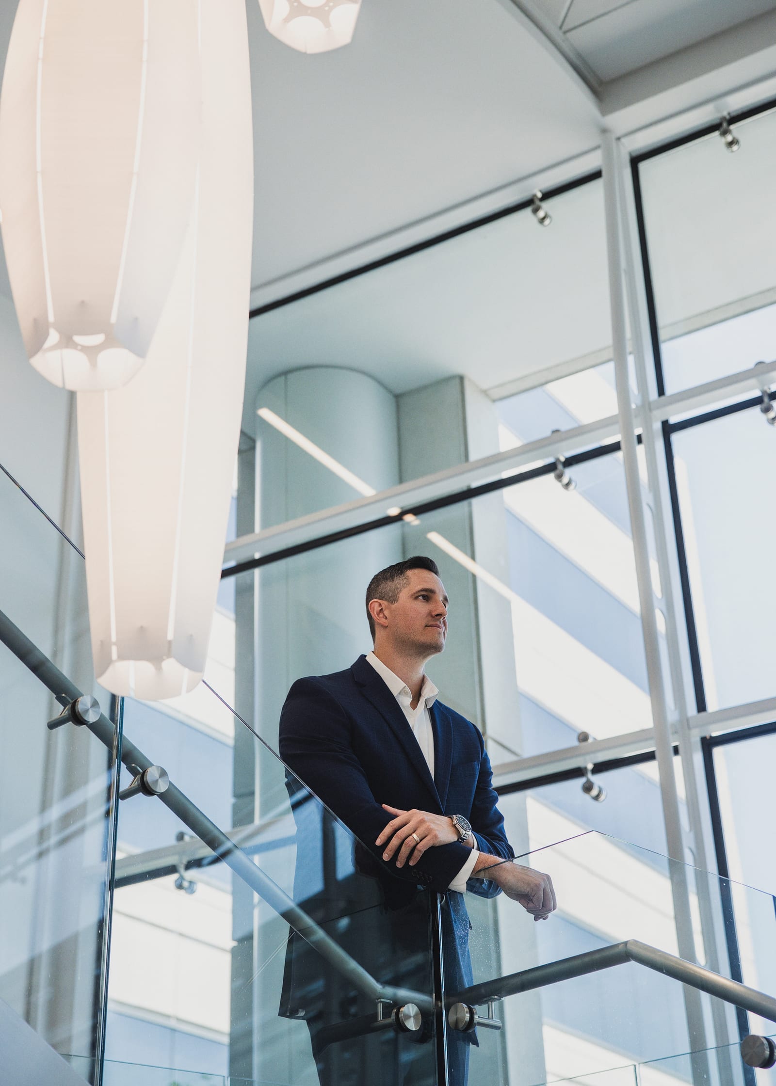 Professional in a dark suit standing at a staircase rail in a bright glass atrium